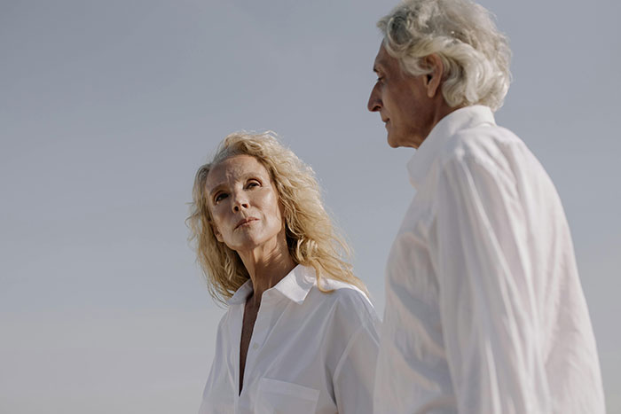 Elderly couple in white shirts, standing against a clear sky, looking contemplative. Elderly couple in white shirts, standing against a clear sky, looking contemplative.