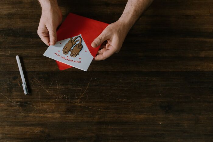 Person holding a Valentine's Day card on a wooden table, illustrating white lies that totally backfired on them.