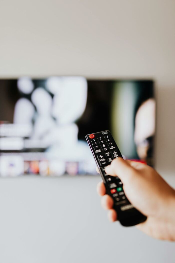 Hand holding TV remote pointed at blurred television screen, illustrating moments when white lies backfired unexpectedly.