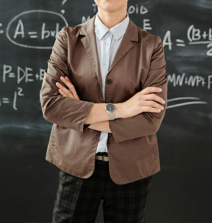 Person in brown blazer standing confidently with arms crossed in front of a chalkboard, illustrating white lies backfiring scenarios.