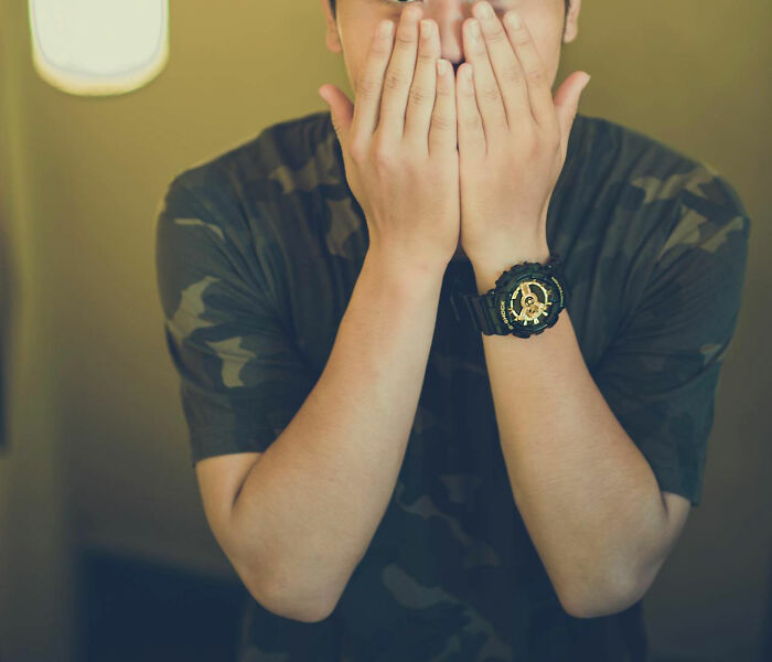 Person in camouflage shirt covering their face with hands, illustrating white lies that totally backfired on them.