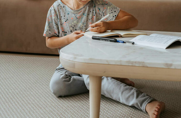 Child sitting on carpet and writing in notebook with pen and marker on table, illustrating white lies backfiring moments.