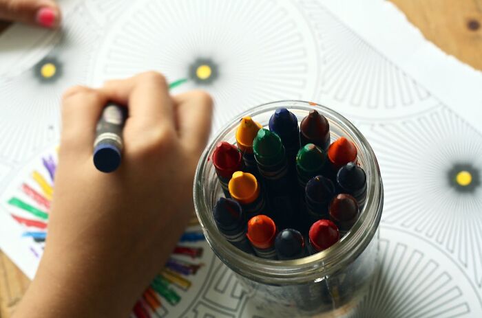 Child’s hand coloring a detailed design with crayons, illustrating moments when white lies totally backfired on people.
