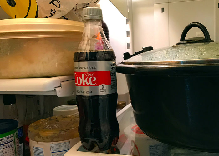 Plastic bottle of Diet Coke inside a fridge with various food items illustrating food thieves at work lessons.