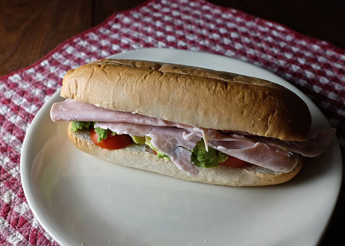 Ham sandwich on a white plate with lettuce and tomato, illustrating a lesson about food thieves at work.