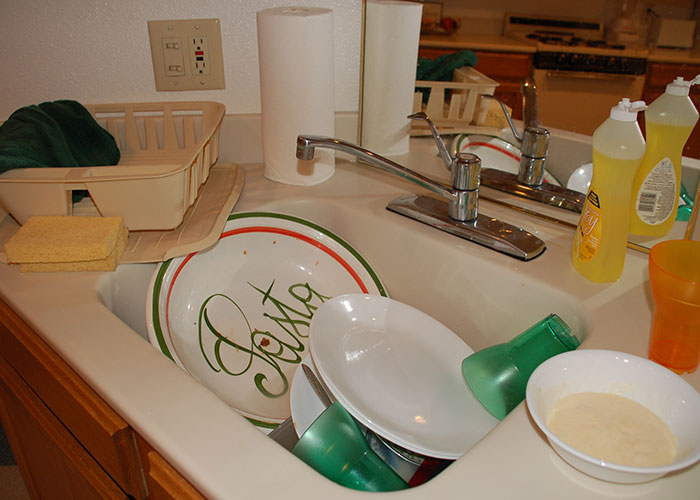 Kitchen sink filled with dirty dishes and utensils, illustrating a common food thieves at work scenario.