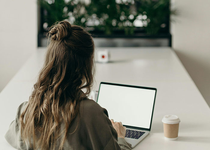 Woman with long hair working on a laptop at a white desk with coffee, illustrating food thieves at work lesson concept.