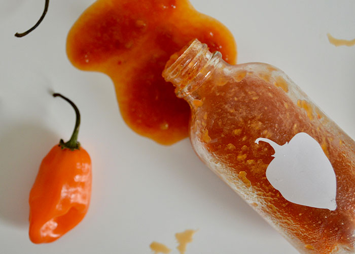 Spilled hot sauce bottle and two hot peppers symbolizing spicy food as a lesson for food thieves at work.