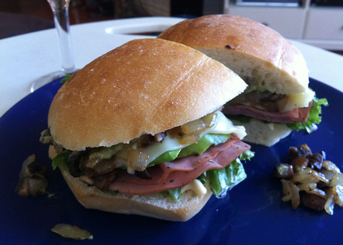 Two ham and cheese sandwiches with lettuce and grilled onions on a blue plate, illustrating food thieves at work lessons.