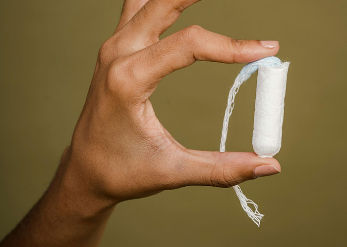 Hand holding a white tampon against a plain background, unrelated to food thieves at work lessons.