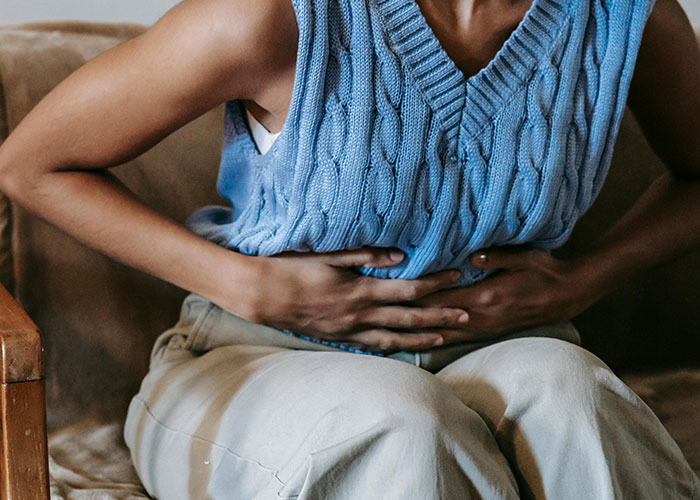 Person in a blue knit vest sitting on a couch holding their stomach, illustrating things people believed were normal until the truth