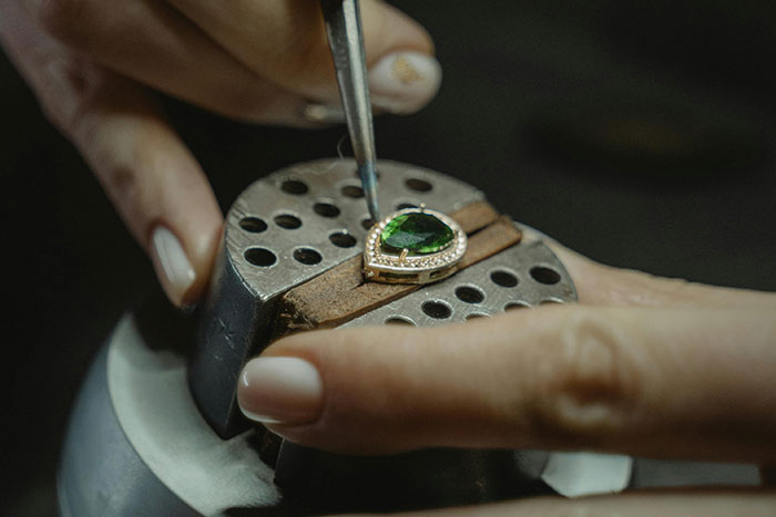 Craftsman setting a large green gemstone into a luxury ring, highlighting things ultra rich individuals can afford to do.