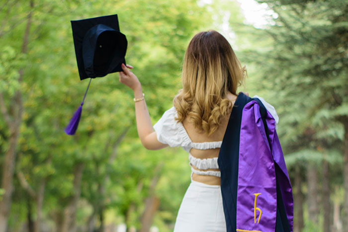 Young woman holding graduation cap and robe outdoors, symbolizing people with insider information on ultra rich individuals.