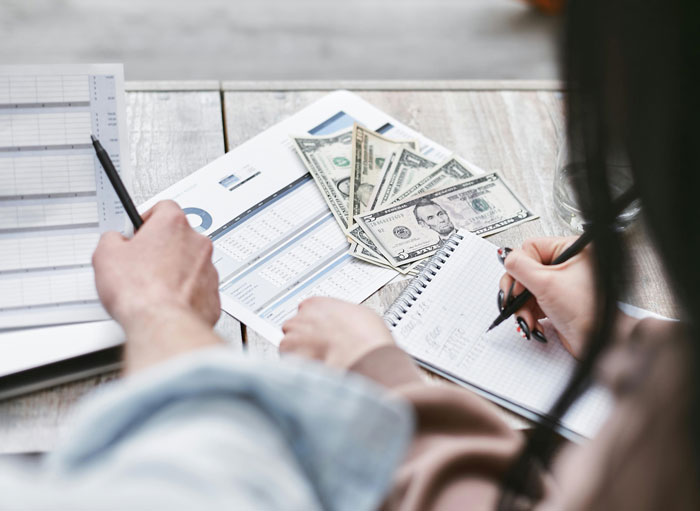 Two people reviewing financial documents and taking notes, with cash on the table.