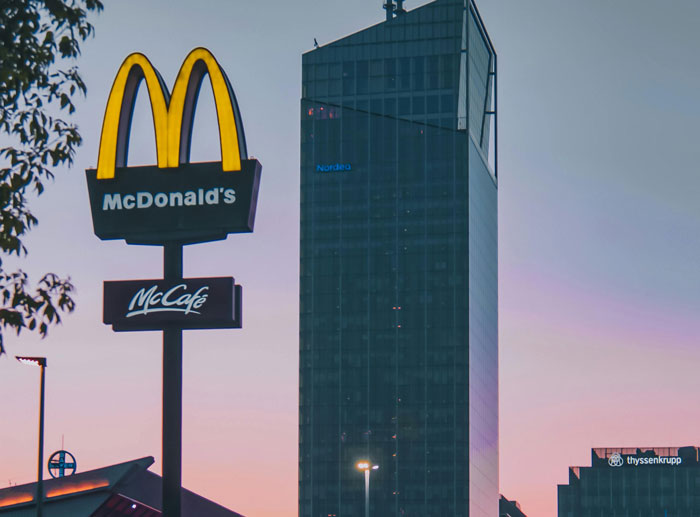 McDonald’s sign and McCafé logo near a tall office building at dusk in an urban cityscape.