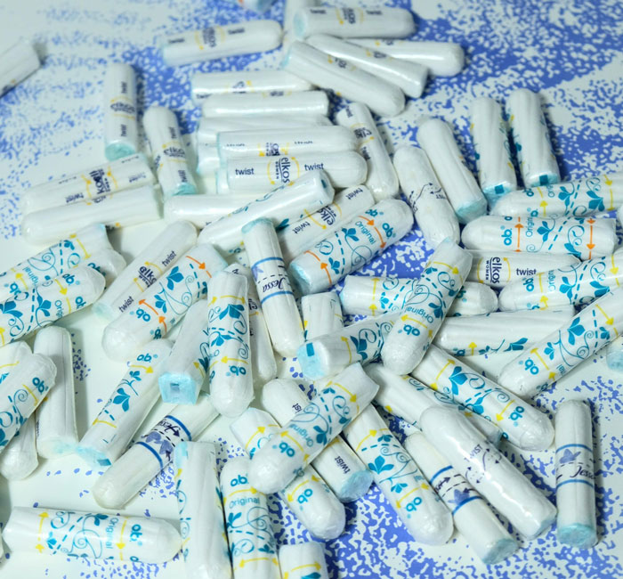 Tampons with various brand wrappers scattered on a blue and white speckled surface showing feminine hygiene products.