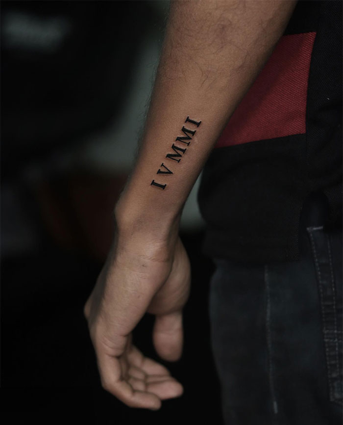  A tattoo on the inner forearm featuring Roman numerals "IV MMXI." A simple and sleek tattoo idea for men, symbolizing a significant date or event in a bold yet minimal style.