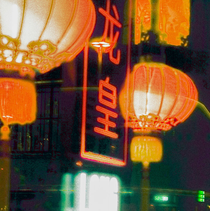 Glowing red lanterns and neon signs illuminating a street scene at night, highlighting village life and culture.