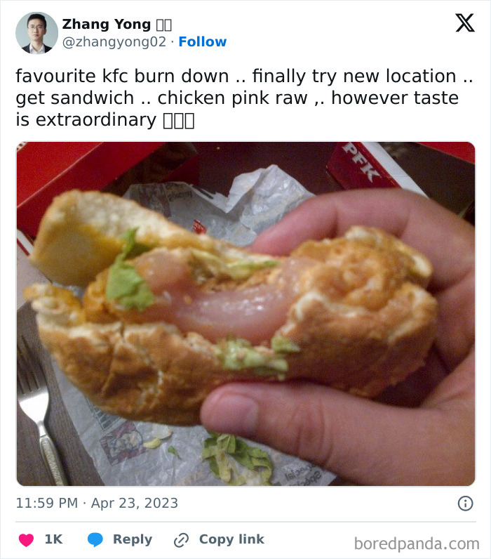 Close-up of a hand holding a fried chicken sandwich with raw pink chicken inside, illustrating sadistic meme humor.