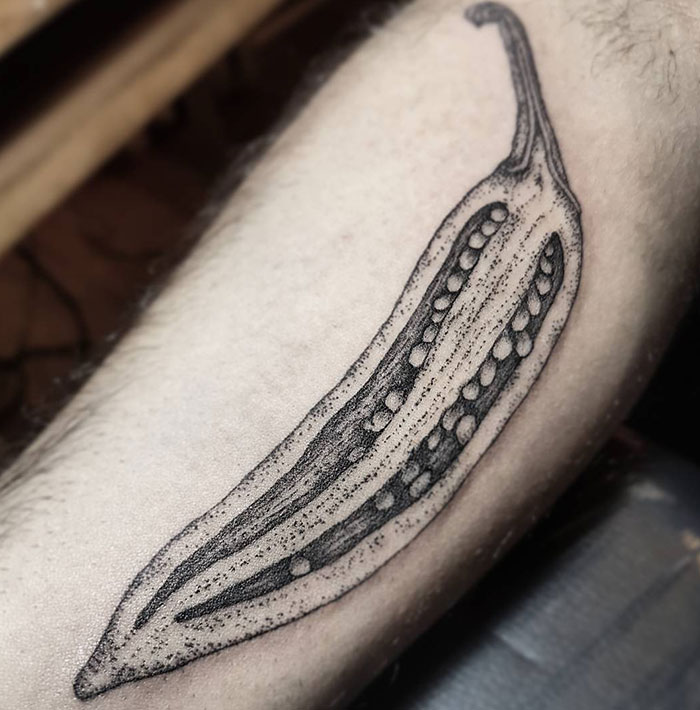 Minimalistic tattoo ideas for men featuring a detailed black-ink drawing of a sliced okra pod, showcasing its seeds and texture with subtle dot shading for a unique botanical design.