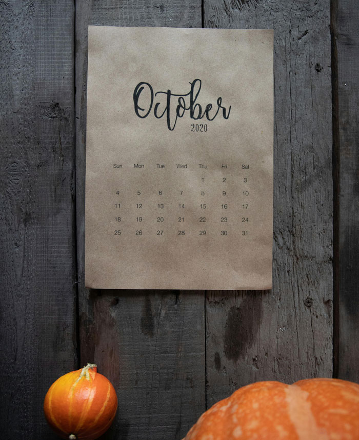 October 2020 calendar on rustic wooden wall with small pumpkins, related to stories about Kevin and village deprivation.
