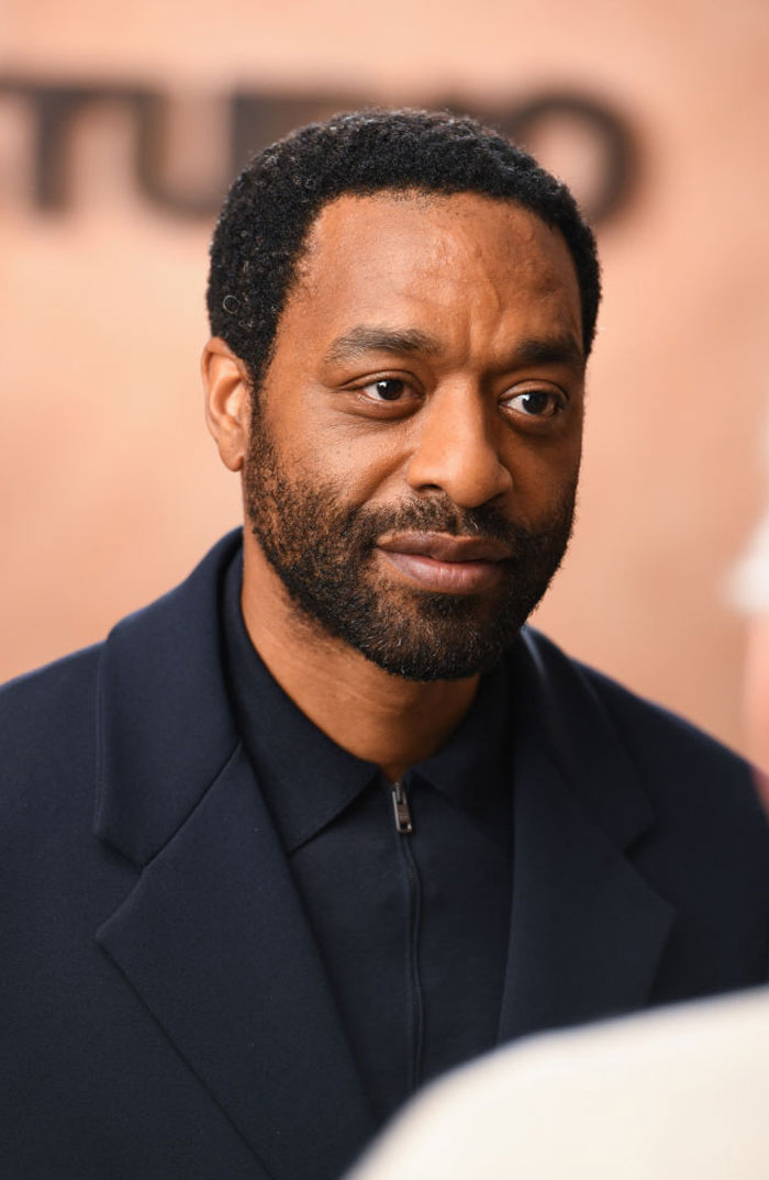 A B list celebrity, Chiwetel Ejiofor, is pictured wearing a dark coat and looking thoughtfully during an indoor event, with a blurred background behind him.