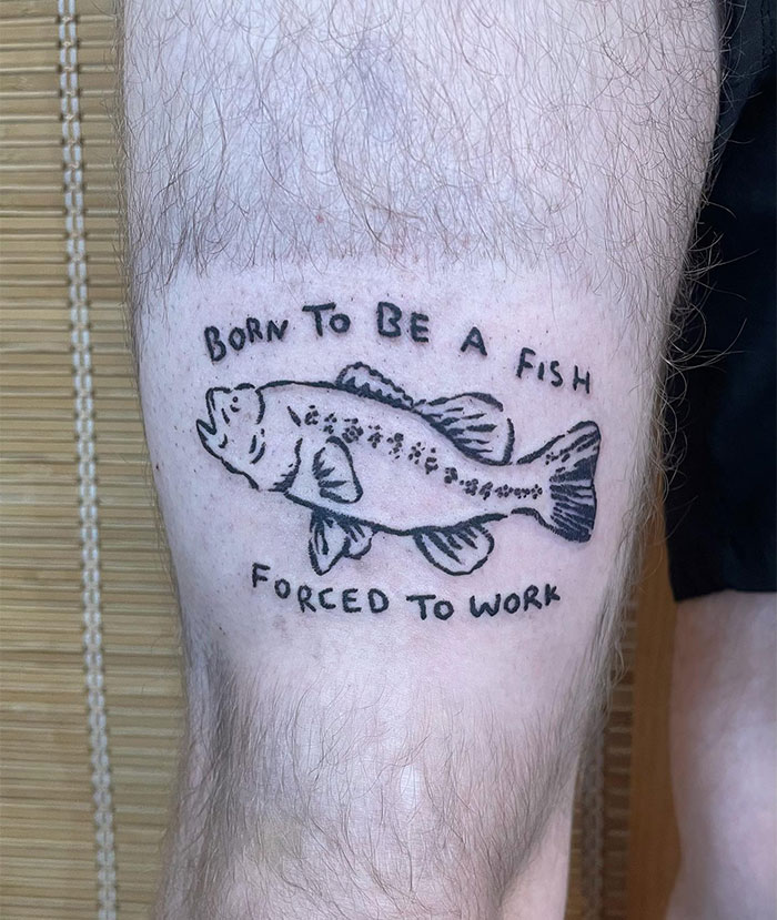 Humorous tattoo ideas for men featuring a simple line-drawn fish with the phrase "Born to be a fish, forced to work," capturing a playful and relatable message with minimalist black ink.