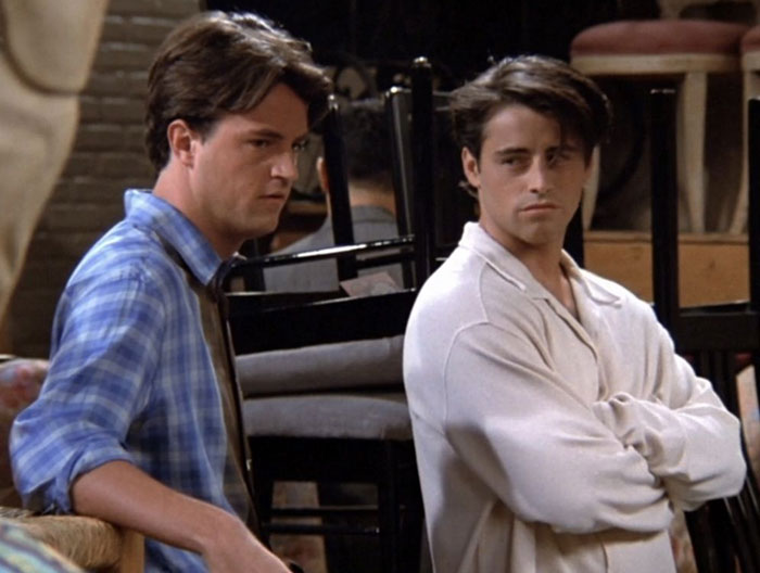 Two iconic TV characters sitting in a café, one wearing a blue shirt, the other a white shirt, showcasing iconic duos.