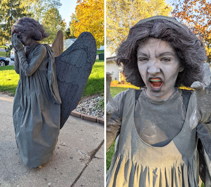 Child dressed as a stone angel statue Halloween costume, covered in gray makeup and wearing wings outdoors in fall.