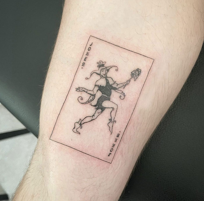  Vintage tattoo ideas for men featuring a detailed linework design of a classic Joker playing card, with a jester in dynamic motion holding a mask, capturing a timeless and artistic look.