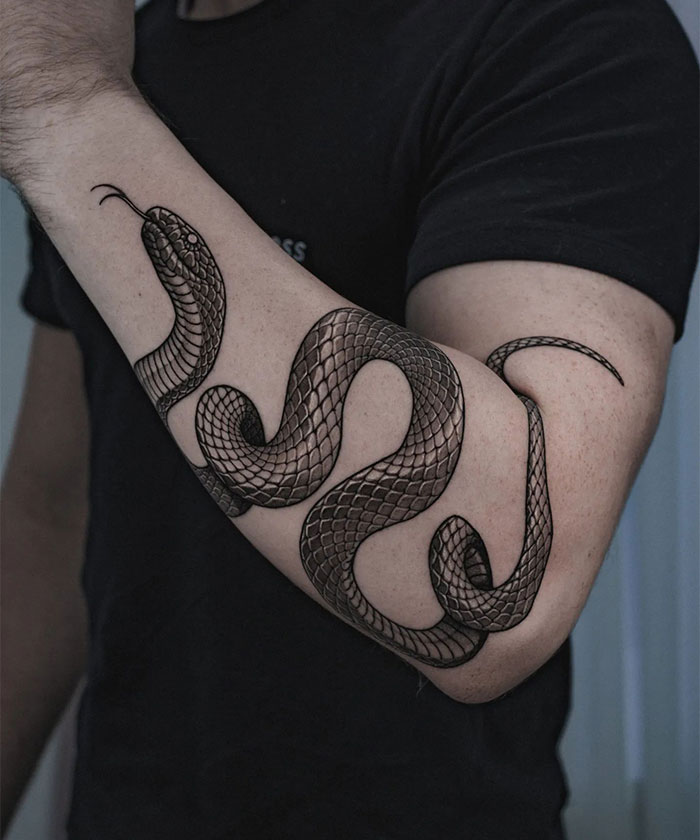  Bold tattoo ideas for men featuring a realistic black ink snake coiling around the forearm, detailed with intricate scales and shading to create a striking and lifelike effect.