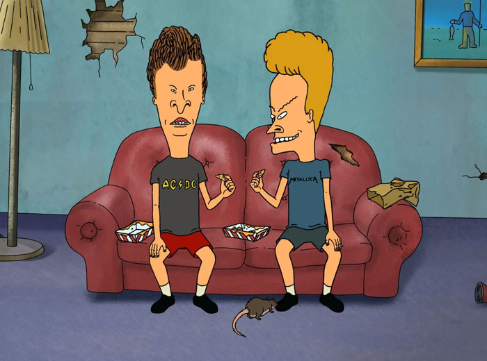 Iconic animated duo sitting on a couch, eating snacks, with a rat on the floor nearby.