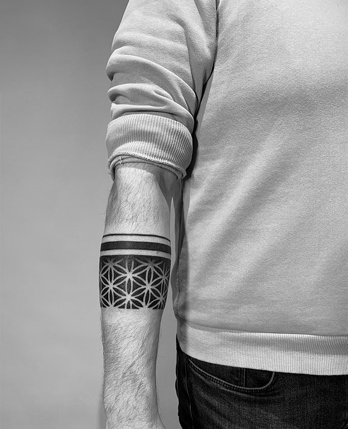  Geometric tattoo ideas for men featuring a forearm band with bold solid lines and intricate patterns resembling a flower of life design, creating a modern and symmetrical look.