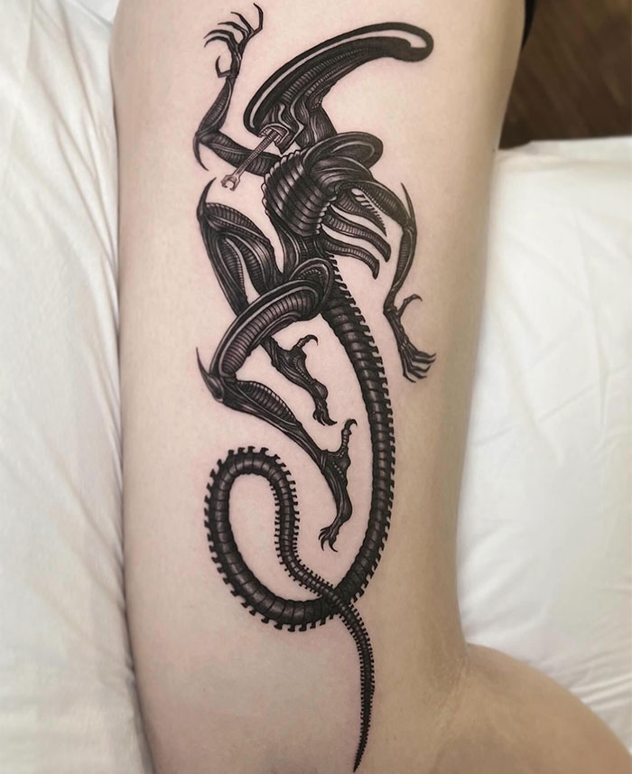  Sci-fi inspired tattoo ideas for men featuring a detailed black ink design of a futuristic alien creature with a sleek, biomechanical body and curved tail, creating a bold and dynamic look.