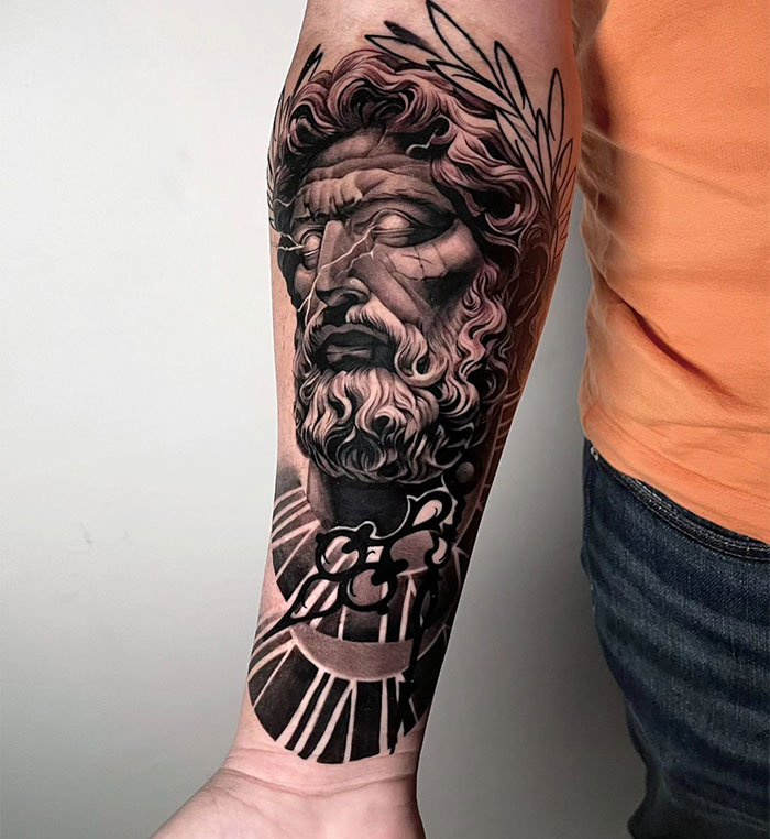  Detailed tattoo ideas for men featuring a classical Greek statue-inspired design with intricate shading, portraying a bearded god-like figure, laurel wreath, and geometric patterns.