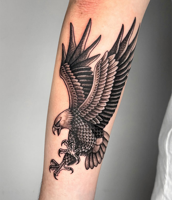 A detailed black and gray tattoo of an eagle with outstretched wings and sharp talons in a diving pose, showcasing bold shading and line work. Ideal for tattoo ideas for men.