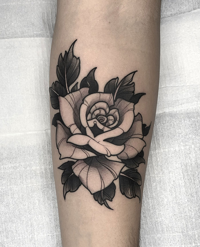 A detailed black and grey rose tattoo on the leg with bold leaves and shading, offering classic and stylish tattoo ideas for men.