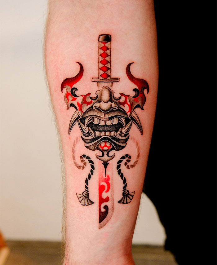 Samurai-inspired tattoo ideas for men featuring a forearm design with a detailed mask and a sword, accented with red flames and intricate patterns for a bold look.