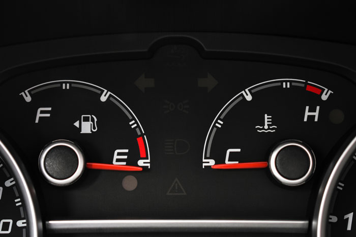 Car dashboard close-up showing fuel gauge near empty and engine temperature gauge at cold, highlighting vehicle status.