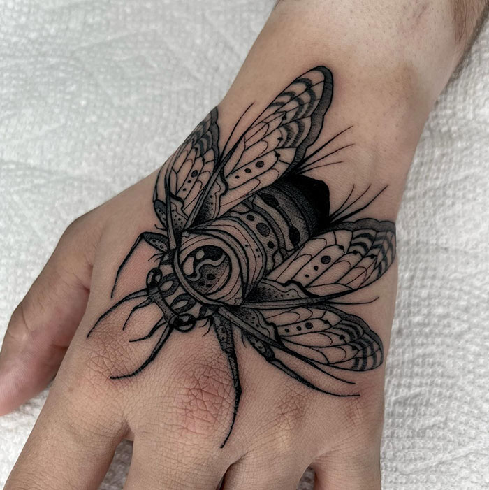 A detailed black ink tattoo of a moth on the back of the hand, showcasing intricate wing patterns and shading. It offers bold and stylish tattoo ideas for men looking for hand tattoos.