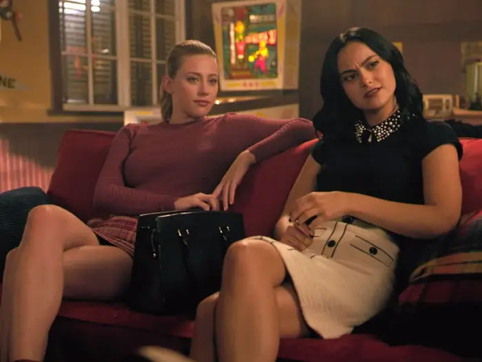 Two women sitting on a red couch, representing iconic duos, in a cozy room setting.