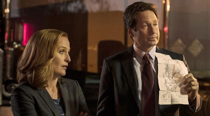 Two iconic characters standing together, one holding a sketch, in front of a dimly lit background.