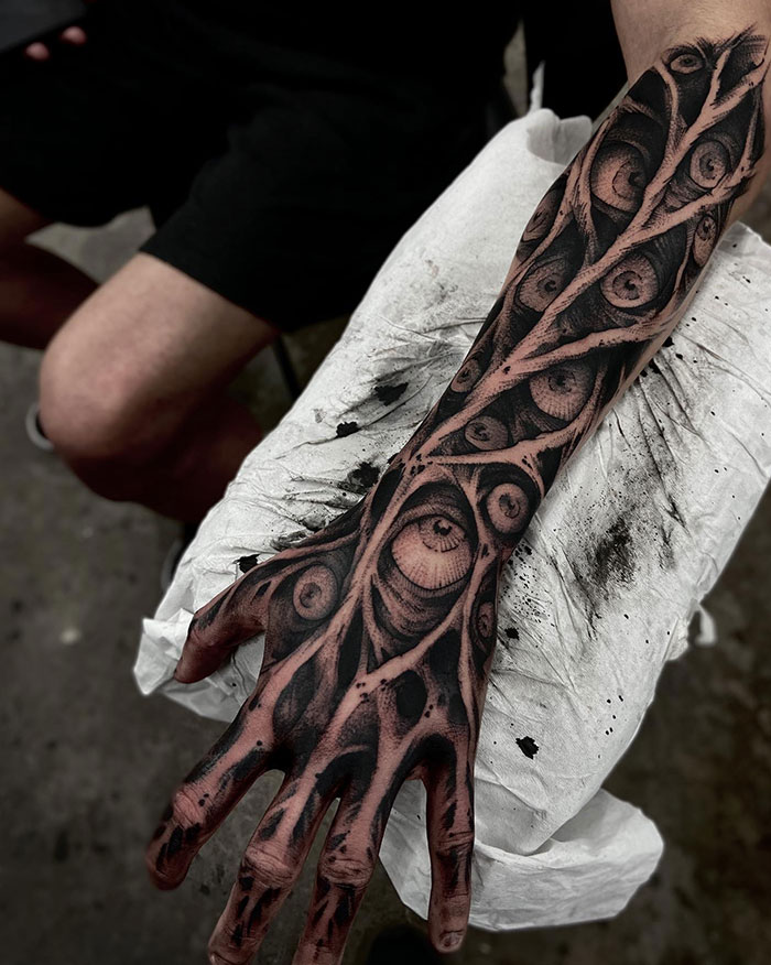  A surreal black and grey full-arm tattoo with intricate designs of eyes embedded within organic branches, presenting unique and edgy tattoo ideas for men.