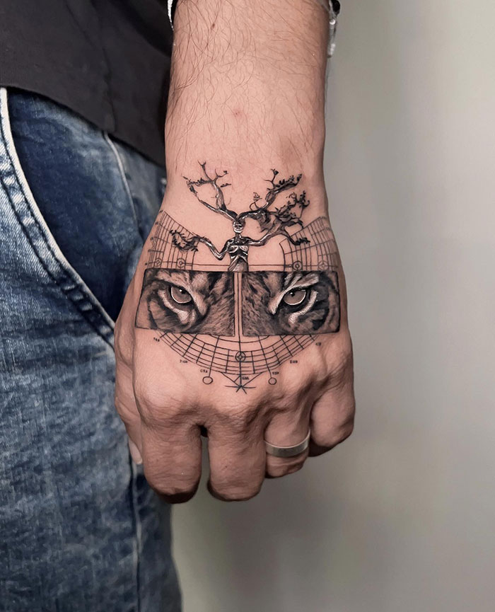 A detailed black and grey hand tattoo featuring the intense eyes of a tiger with branches growing upward, accompanied by geometric elements, offering bold and unique tattoo ideas for men.