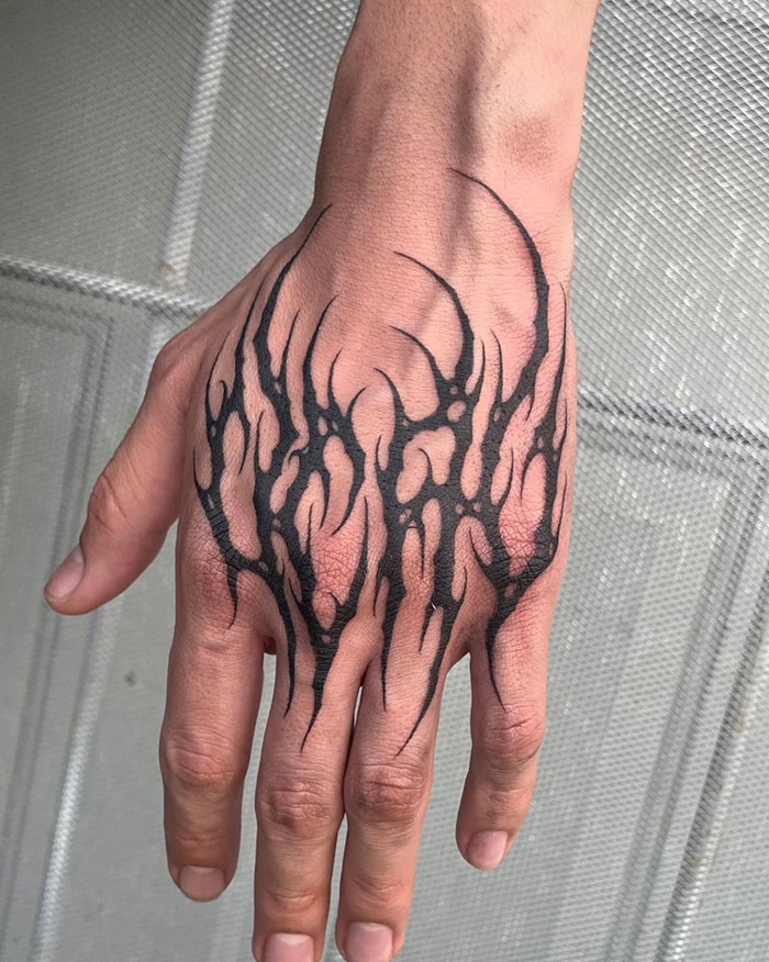  Black abstract hand tattoo with flame-like designs stretching across the knuckles, providing bold and edgy tattoo ideas for men.
