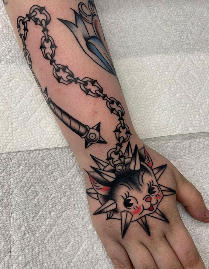  A creative tattoo featuring a playful cat head stylized as a medieval flail with spikes and a chain wrapping around the wrist, offering unique tattoo ideas for men.