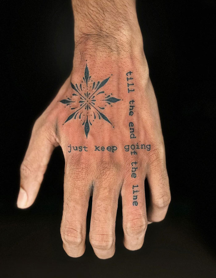  A minimalist hand tattoo featuring a star-shaped pattern in the center with the motivational phrase "just keep going till the end of the line" written along the fingers, offering simple yet meaningful tattoo ideas for men.
