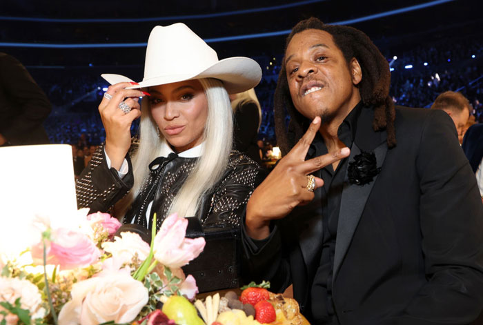 Two iconic figures at an event, with one wearing a white hat, surrounded by flowers and lights.