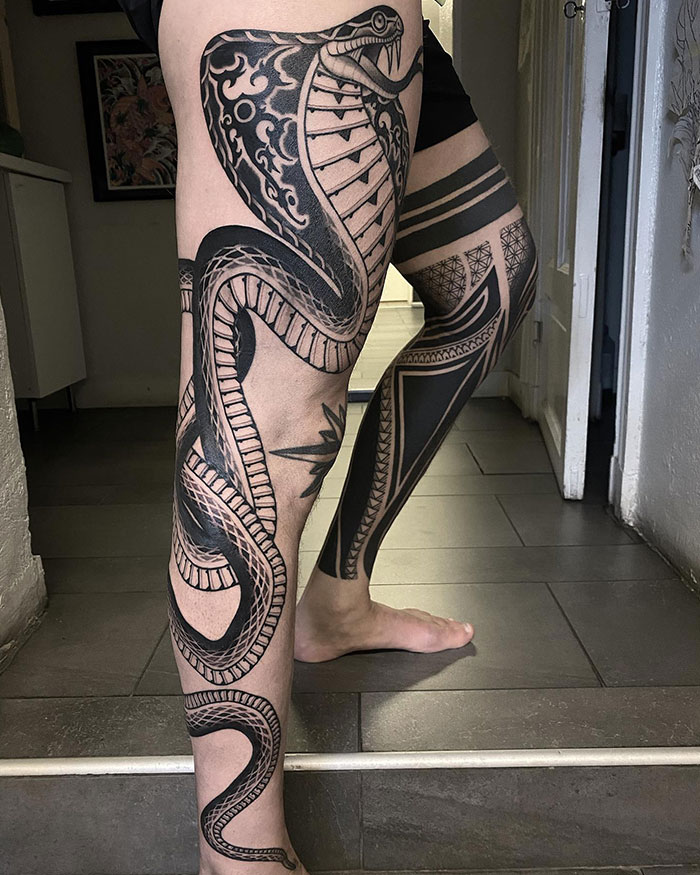  A leg tattoo featuring a large, intricately designed cobra snake wrapping around the leg, combined with bold geometric patterns, offering bold and detailed tattoo ideas for men seeking a fierce look.