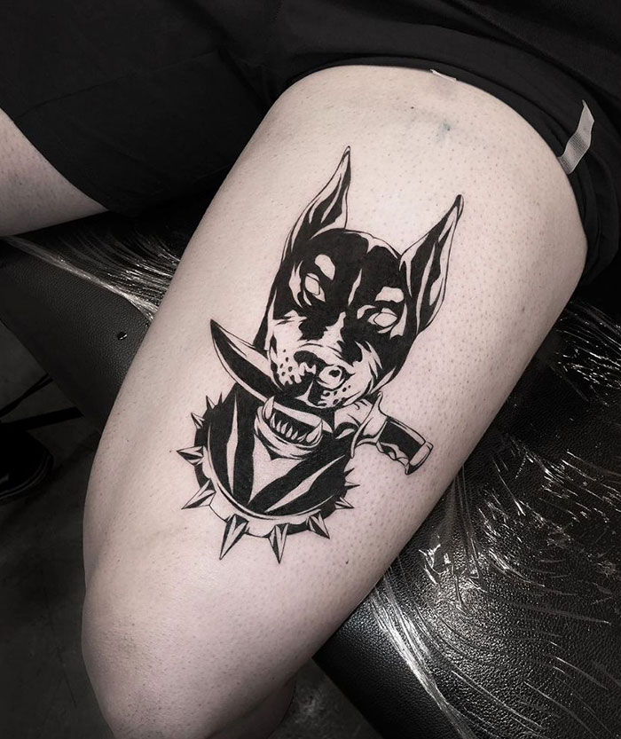  A bold thigh tattoo featuring a menacing Doberman wearing a spiked collar and holding a knife in its mouth, offering fierce and edgy tattoo ideas for men.
